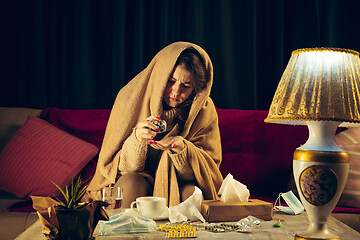 Image showing Woman wrapped in a plaid looks sick, ill, sneezing and coughing sitting at home indoors