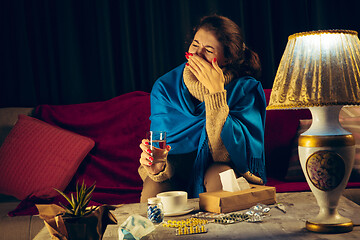 Image showing Woman wrapped in a plaid looks sick, ill, sneezing and coughing sitting at home indoors