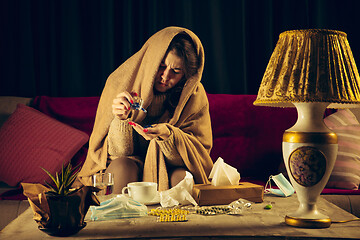 Image showing Woman wrapped in a plaid looks sick, ill, sneezing and coughing sitting at home indoors