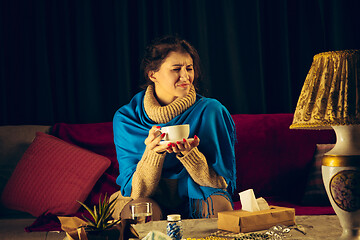 Image showing Woman wrapped in a plaid looks sick, ill, sneezing and coughing sitting at home indoors