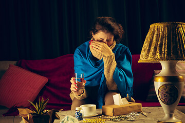 Image showing Woman wrapped in a plaid looks sick, ill, sneezing and coughing sitting at home indoors