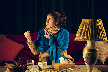 Image showing Woman wrapped in a plaid looks sick, ill, sneezing and coughing sitting at home indoors