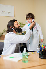 Image showing Paediatrician doctor examining a child while wearing face mask in comfortabe medical office