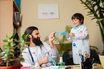 Image showing Paediatrician doctor examining a child while wearing face mask in comfortabe medical office