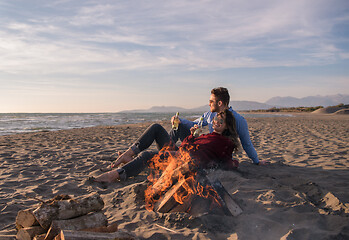 Image showing Young Couple Sitting On The Beach beside Campfire drinking beer