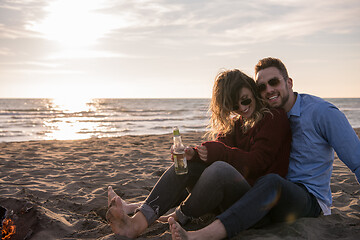 Image showing Young Couple Sitting On The Beach beside Campfire drinking beer