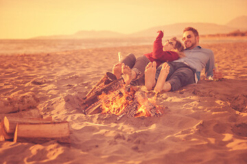 Image showing Young Couple Sitting On The Beach beside Campfire drinking beer