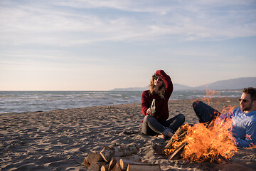 Image showing Young Couple Sitting On The Beach beside Campfire drinking beer