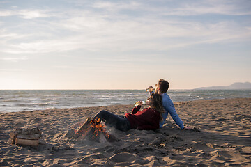 Image showing Young Couple Sitting On The Beach beside Campfire drinking beer