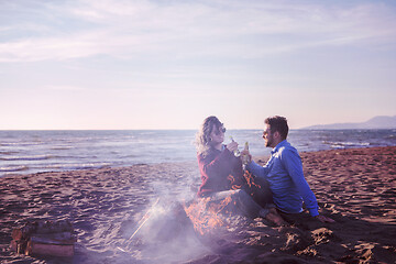 Image showing Young Couple Sitting On The Beach beside Campfire drinking beer