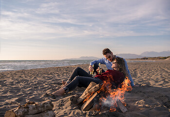 Image showing Young Couple Sitting On The Beach beside Campfire drinking beer