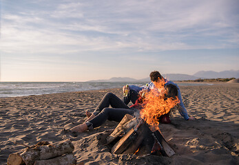 Image showing Young Couple Sitting On The Beach beside Campfire drinking beer