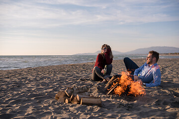 Image showing Young Couple Sitting On The Beach beside Campfire drinking beer