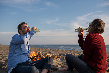 Image showing Young Couple Sitting On The Beach beside Campfire drinking beer