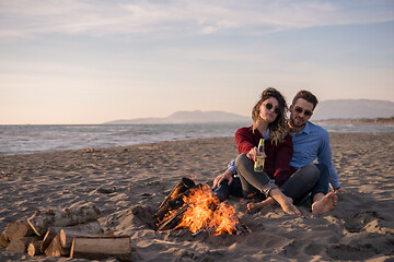 Image showing Young Couple Sitting On The Beach beside Campfire drinking beer