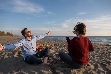 Image showing Young Couple Sitting On The Beach beside Campfire drinking beer