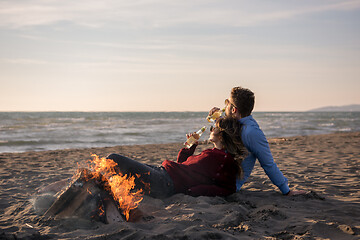 Image showing Young Couple Sitting On The Beach beside Campfire drinking beer