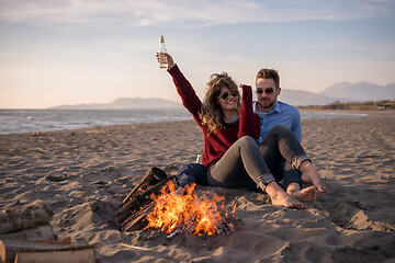 Image showing Young Couple Sitting On The Beach beside Campfire drinking beer