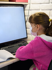 Image showing A girl in a medical mask sits at a computer and learns online