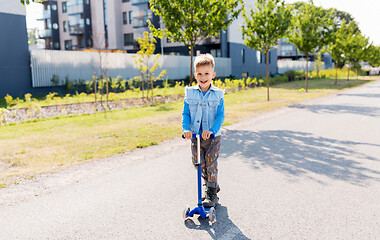 Image showing happy little boy riding scooter in city