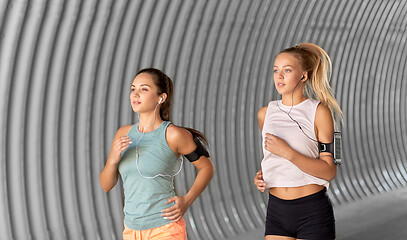 Image showing young women with earphones and smartphones running