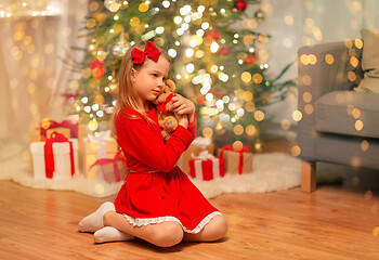 Image showing girl in red dress hugging teddy bear at home