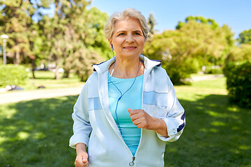 Image showing senior woman with earphones running at summer park