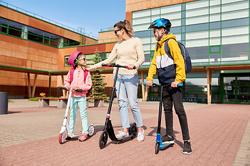 Image showing happy school children with mother riding scooters