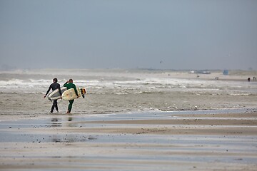 Image showing Surfers entering the water in cold windy weather