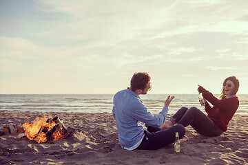 Image showing Young Couple Sitting On The Beach beside Campfire drinking beer