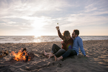 Image showing Young Couple Sitting On The Beach beside Campfire drinking beer