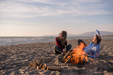 Image showing Young Couple Sitting On The Beach beside Campfire drinking beer