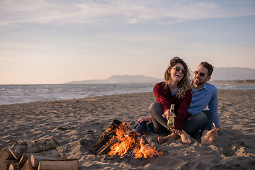 Image showing Young Couple Sitting On The Beach beside Campfire drinking beer