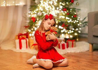 Image showing girl in red dress hugging teddy bear at home