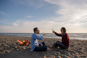 Image showing Young Couple Sitting On The Beach beside Campfire drinking beer