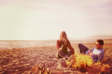 Image showing Young Couple Sitting On The Beach beside Campfire drinking beer