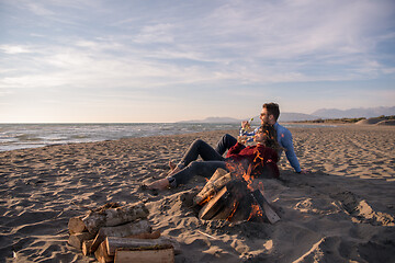 Image showing Young Couple Sitting On The Beach beside Campfire drinking beer