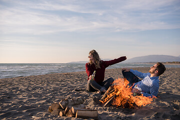 Image showing Young Couple Sitting On The Beach beside Campfire drinking beer