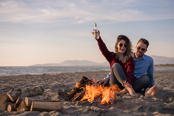 Image showing Young Couple Sitting On The Beach beside Campfire drinking beer