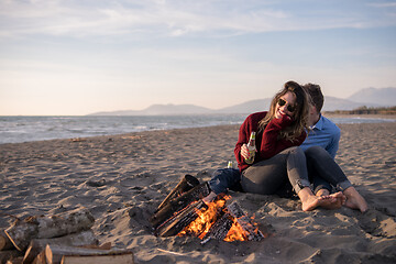 Image showing Young Couple Sitting On The Beach beside Campfire drinking beer