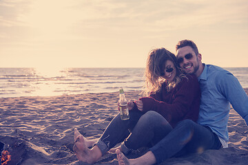 Image showing Young Couple Sitting On The Beach beside Campfire drinking beer