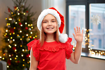 Image showing happy girl in santa helper hat waving hand at home