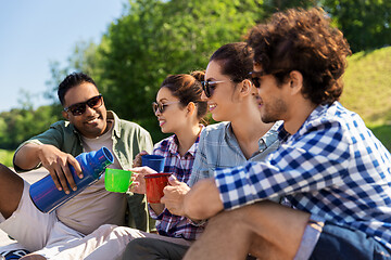 Image showing happy friends drinking tea from thermos in summer