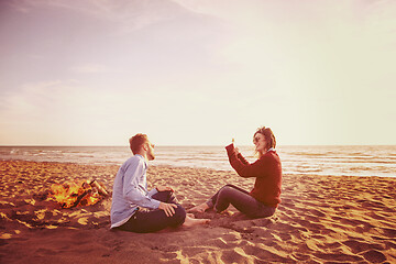 Image showing Young Couple Sitting On The Beach beside Campfire drinking beer