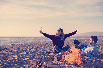 Image showing Young Couple Sitting On The Beach beside Campfire drinking beer