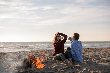 Image showing Young Couple Sitting On The Beach beside Campfire drinking beer