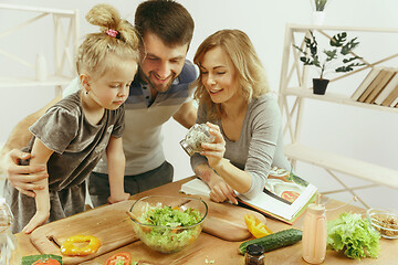 Image showing Cute little girl and her beautiful parents are cutting vegetables in kitchen at home