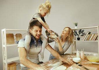 Image showing Cute little girl and her beautiful parents preparing the dough for the cake in kitchen at home