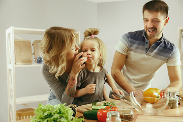 Image showing Cute little girl and her beautiful parents are cutting vegetables in kitchen at home