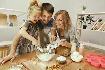 Image showing Cute little girl and her beautiful parents preparing the dough for the cake in kitchen at home